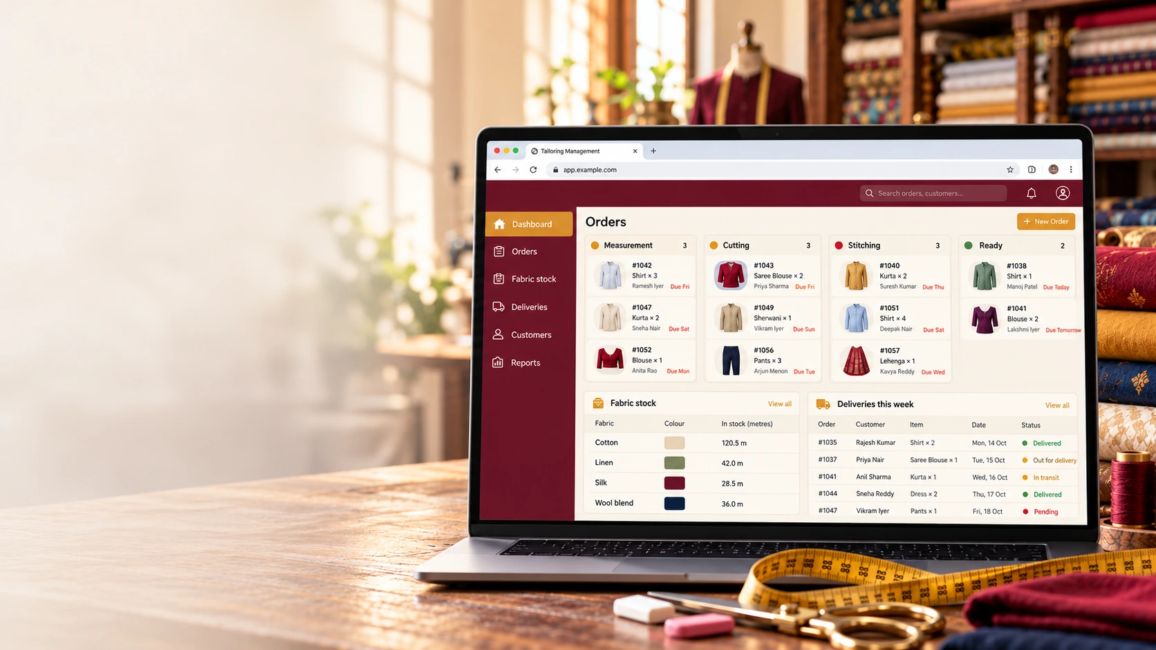 Laptop on a tailor's table among maroon and mustard fabric, showing the order board from measurement to ready